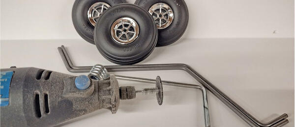 Dremel tool, three model wheels, and metal rods on a white background.
