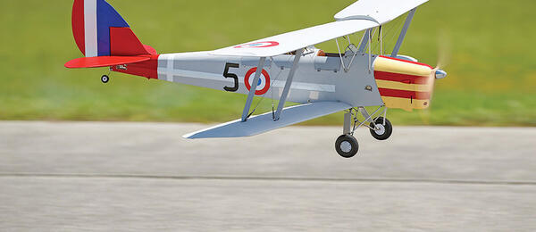 Model biplane with red, white, and blue markings flying close to the ground.
