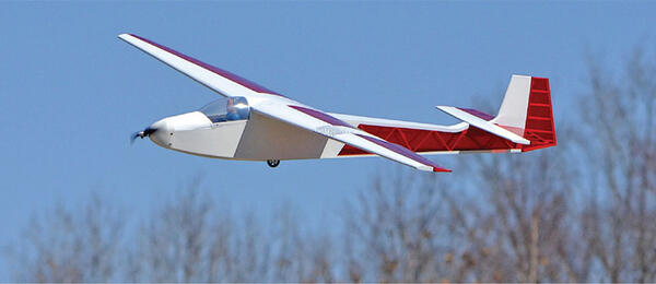 A white and red model glider in flight against a clear blue sky.