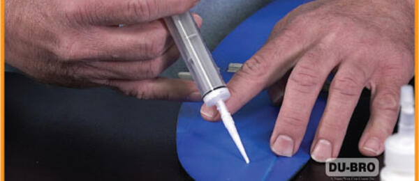 Hands applying glue to a blue object with a syringe; DU-BRO logo visible.