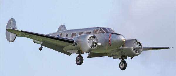 Silver vintage airplane flying in a blue sky.