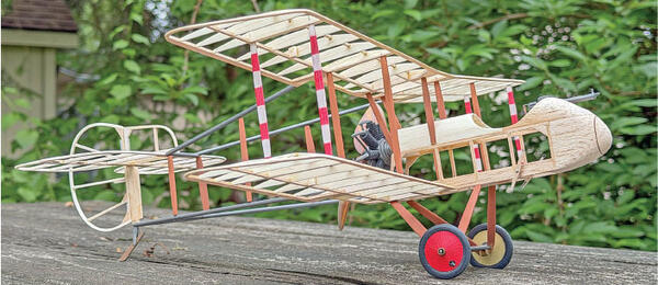 Wooden model biplane on a wooden table, with green foliage in the background.