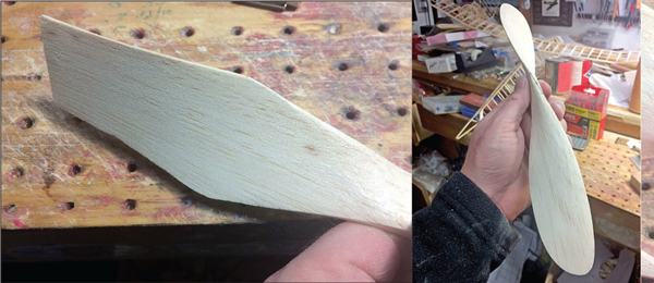 Wooden propeller in a workshop, held in hand against a workbench.