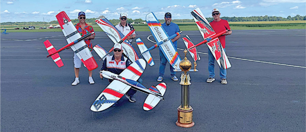 Five people holding model airplanes, a large trophy in front.