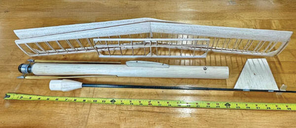 Model airplane wing parts laid on a wooden surface with a tape measure below.