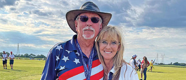 Smiling man in USA flag shirt and woman outdoors under cloudy sky.