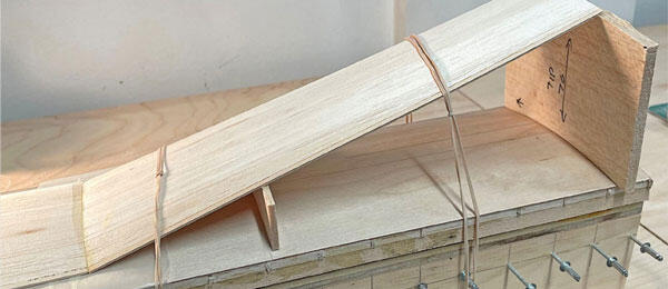 Wooden model bridge with rubber band supports on a table.