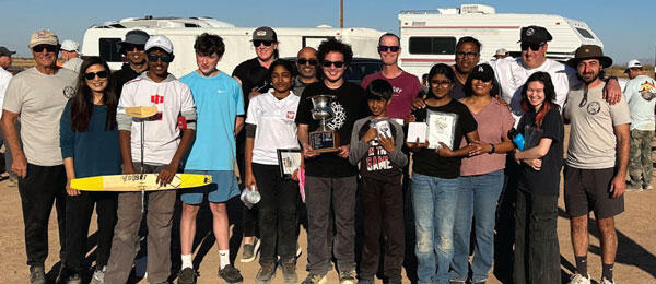 Group of people outdoors holding small trophies and awards, smiling under the sun.