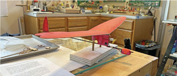 Red model airplane on a workshop table with tools in the background.