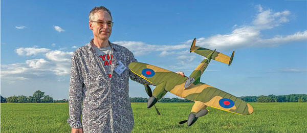 Man holding a model plane with a green field and blue sky in the background.