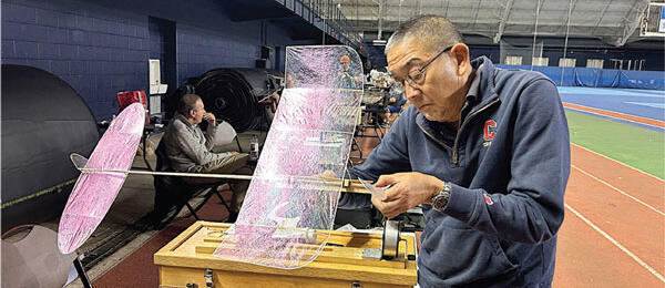 Man adjusting a large, pink model airplane indoors.