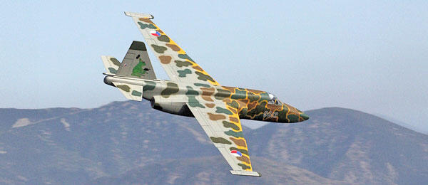 Camouflage fighter jet flying above mountains.