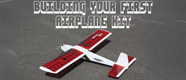 Model airplane with red wings on asphalt, text reads "Building Your First Airplane Kit".