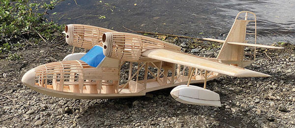 Wooden model seaplane on rocky riverbank with a blue cockpit.
