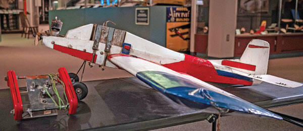 Model airplane displayed indoors, red, white, and blue with a cart attached.