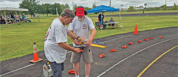 Two men on a track assembling a model aircraft outdoors.