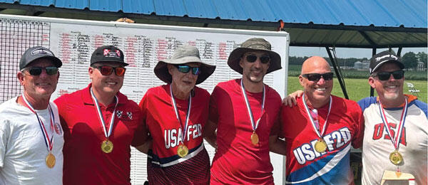 Six men smiling, wearing medals and "USA" shirts, standing under a pavilion.