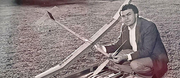 Man crouching on grass, holding a model airplane with tools nearby.
