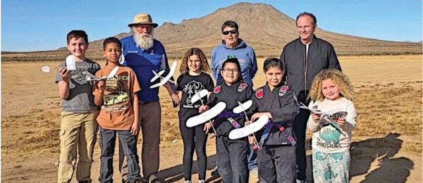 Group with model airplanes in a desert landscape, mountain in background.