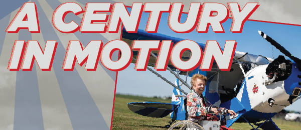 A woman in a wheelchair by a blue airplane with "A Century in Motion" text.