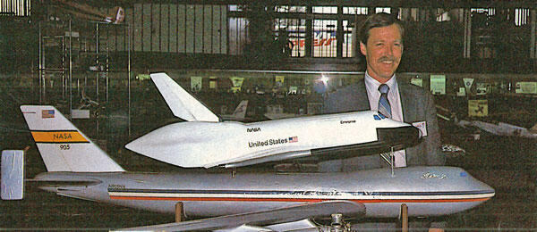 Man smiling next to a model of a space shuttle on a jumbo jet.
