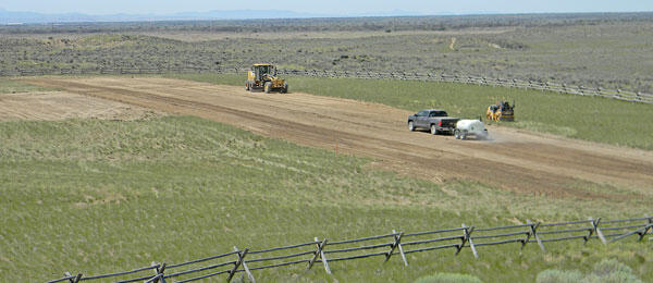Site construction in a rural field with two cars and a distant bulldozer.