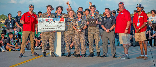 Group of people celebrating with a large check and trophy outdoors.