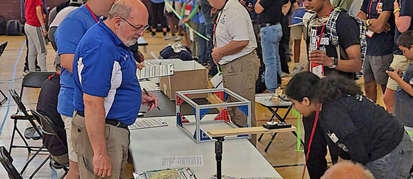 People gathered around tables with projects in a busy hall.
