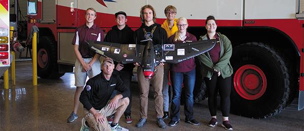 Group of people posing with a model plane in front of a large red and white vehicle.