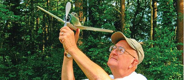 Person throwing a model glider in a grassy field.