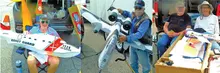 Three men display model airplanes outdoors.