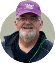 Man smiling, wearing a purple cap with white logo and glasses.