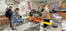 Classroom with teacher and students examining a large model airplane.