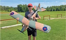 Person holding a large model plane outdoors on a grassy field.