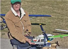 Person holding a model helicopter outside, wearing a jacket and green cap.