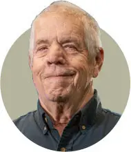 Smiling elderly man in a blue shirt against a neutral background.