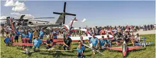 Group with model planes and helicopter at a sunny air show.