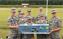 Seven cadets in uniform holding a HobbyZone Aeroscout S 2 1.1m model airplane box outdoors.