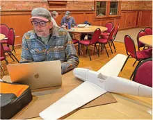 Man working on a laptop next to a model airplane in a room with red chairs.