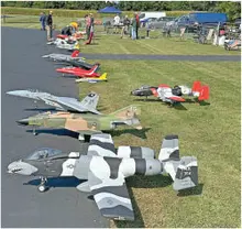 Model aircraft displayed on grass and pavement, people in the background.