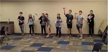 Nine people throw paper airplanes indoors.