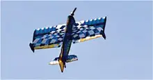 Aerobatic plane flying with checkered wings against blue sky.