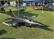 Model jet plane with red details on grass, surrounded by tents and people.