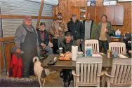 Seven people smiling in a rustic room, with a table and beverages.