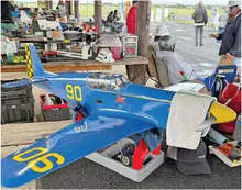 Blue model plane with "90" on wings and fuselage at an outdoor event.