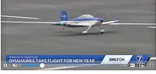 Small blue and white RC plane on runway with news text overlay.