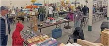 A hobby show with people browsing tables of model airplanes and related items.