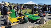 People gathered around a small green and yellow aircraft outdoors.