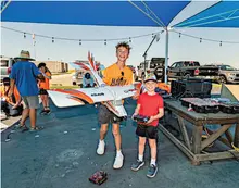 Two smiling boys holding a model airplane and remote, under a blue canopy.
