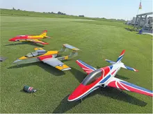 Three colorful model jets on grass near a runway.